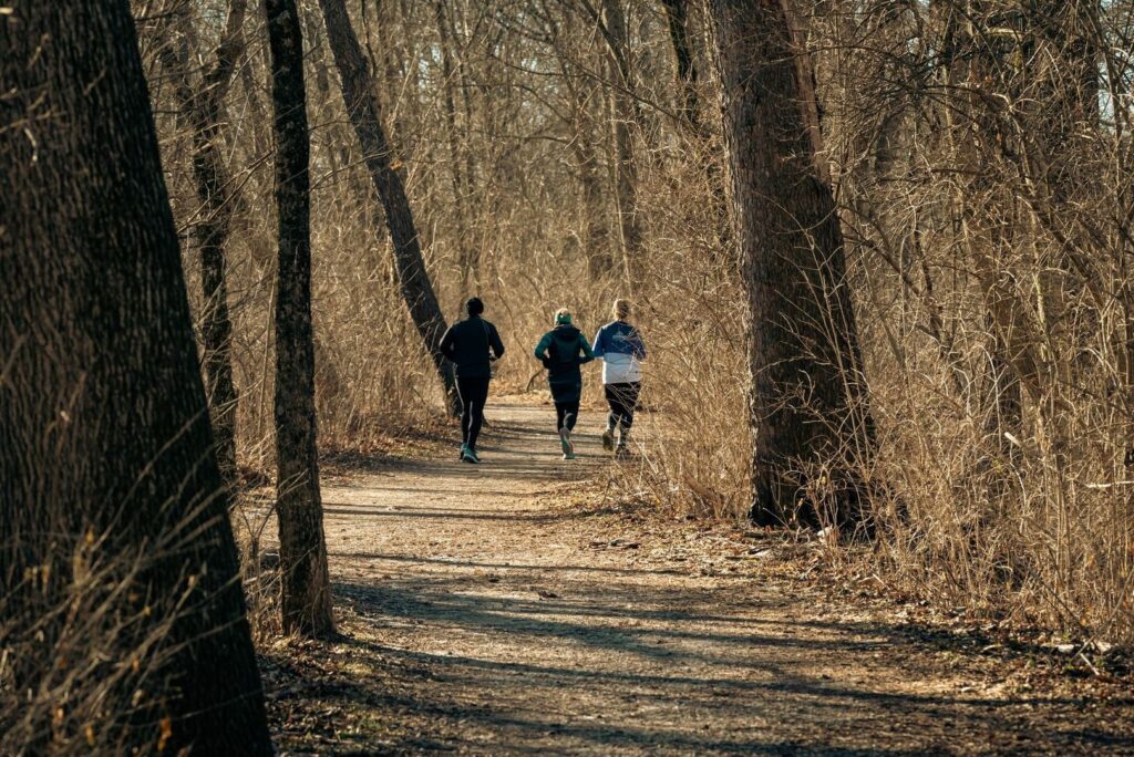 Tre personer joggar på en skogsstig bland täta träd och buskar